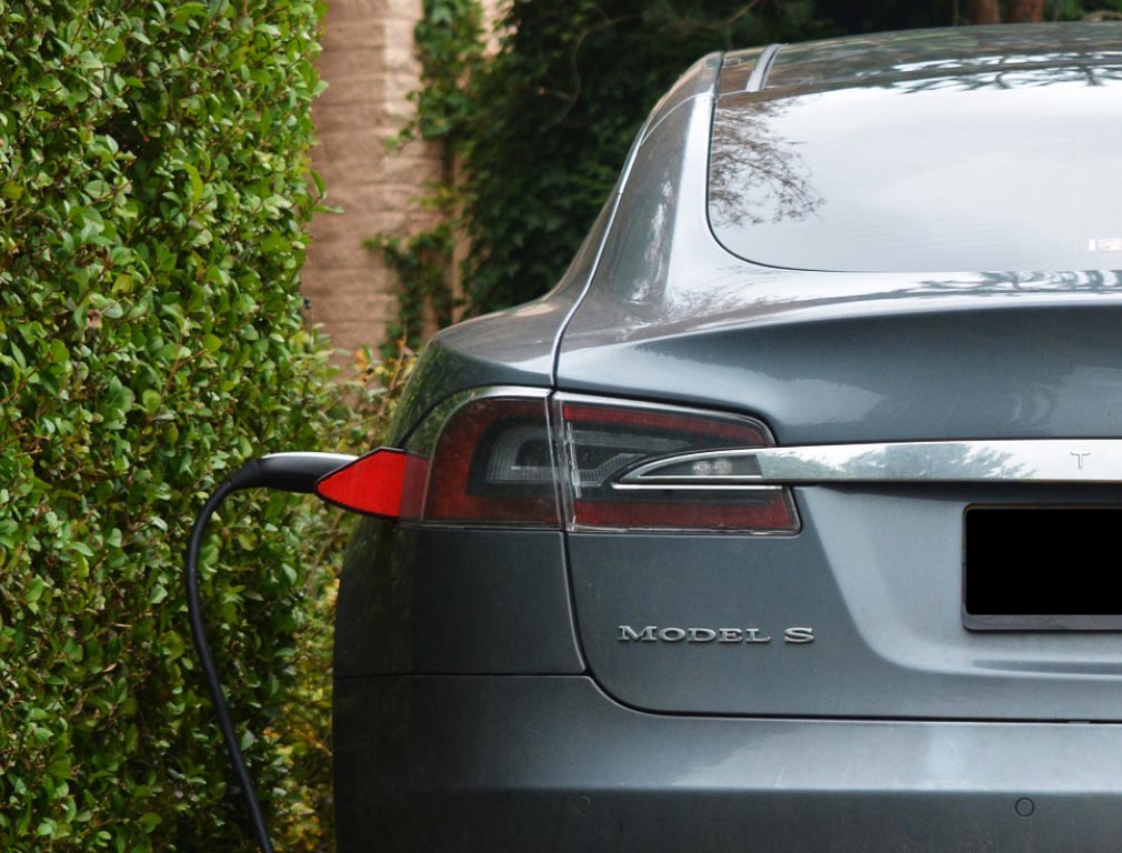 A gray Tesla Model S electric vehicle being charged at a home charging station