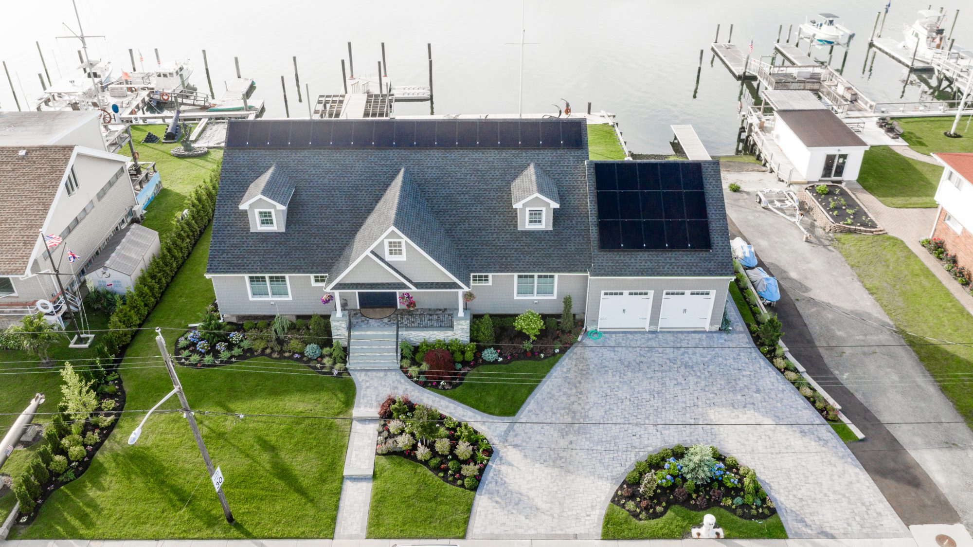 A well-kept house next to the water has solar panels on the roof.