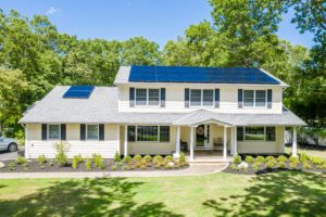 A family home on Long Island that has installed solar panels on the roof. The house is surrounded by beautiful green landscaping.